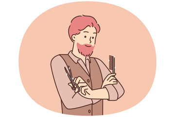 Man hairdresser from beauty salon stands with arms crossed holding comb and scissors