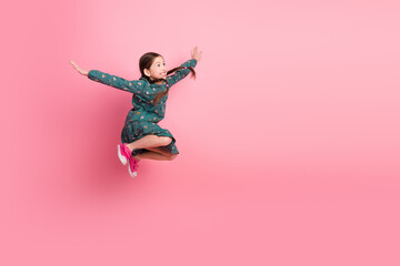 Energetic young girl jumping with enthusiasm and cheer in fashionable outfit on vibrant pink...