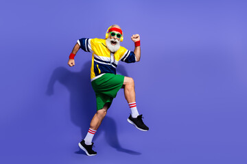 Elderly man wearing vibrant retro sportswear energetically dancing against purple background showcasing active and fit lifestyle