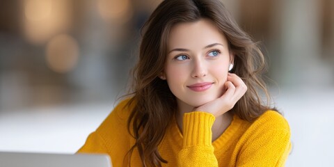 Young woman with brown hair, wearing a yellow sweater, looks thoughtfully off camera, hand gently resting on chin. Soft, natural lighting. Blurred background.