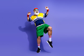 Active senior man in retro sportswear dancing against a colorful background in a fun and energetic pose