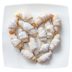 Several croissant-shaped pastries on a plate, arranged in a heart shape and sprinkled with powdered sugar.