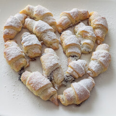 Several croissant-shaped pastries arranged in a heart shape and sprinkled with powdered sugar.