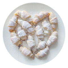 Several croissant-shaped pastries on a plate, arranged in a heart shape and sprinkled with powdered sugar.