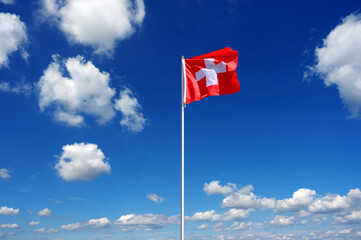 flag of Switzerland fluttering in the blue sky with cumulus clouds