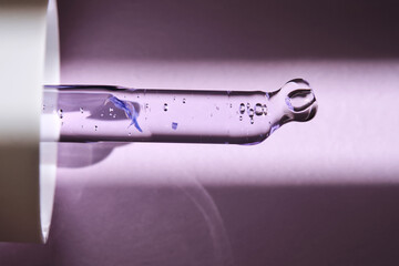 Pipette with serum on purple background with sunlight.
