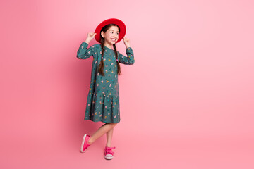 Young girl in a stylish floral dress posing with a red summer hat on a pink background, cheerful and playful