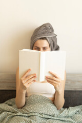 woman with a towel on her head reading a book in bed