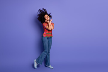 Cheerful young woman dancing energetically against a bold purple background wearing casual stylish outfit