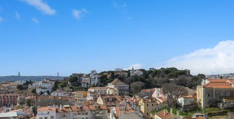 Fototapeta premium Charming Lisbon cityscape with historic buildings and the iconic Castelo de São Jorge under a bright, partly cloudy sky.