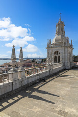 Obraz premium Rooftop view of the historic São Vicente de Fora Monastery in Lisbon, overlooking the Tagus River and cityscape under a bright sky.