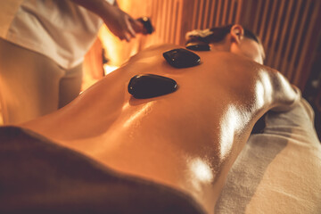 Closeup hot stone massage at spa salon in luxury resort with warm candle light, blissful woman...