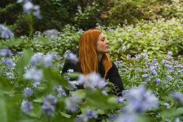 Portrait of redhead woman with closed eyes sitting in perennial honesty flower field in forest