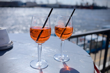 Two glasses of Aperol Spritz with black straw on a table at the harbor with bokeh background