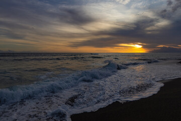 Obraz premium Breathtaking sunset at Bali. Bright sunrise sky against wavy ocean and palm trees, Bali, Indinesia