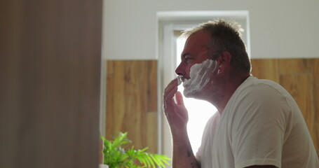 Man applying shaving cream to face, preparing for morning shave, emphasizing self-care and grooming...