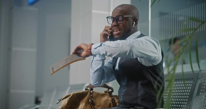 Airport Terminal: African American Entrepreneur Irritated About Flight Delay Talking and Shouting into Phone, Holding Airplane Ticket. Businessman Sitting in Departure Lounge, Going on Business Trip.