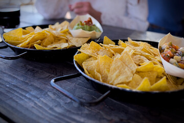 Tortilla nachos in a black cast iron pan with a dip on a wooden table in a restaurant