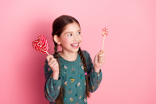 Smiling young girl holding colorful lollipops on a pink backdrop depicting joy, childhood, and sweet treats