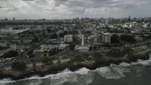 Drone flies north from over rocky waters to the Monument to the Heroes of Constance, Maimon and Estero Hondo and the Centro de los Heroes in Santo Domingo, Dominican Republic