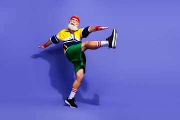 Elderly man in vibrant retro sportswear demonstrating fitness exercises against bold purple...