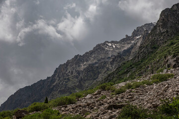 Wide angle landscape high rocky mountain range and glacier peaks and heavy dark storm clouds over, severe weather.