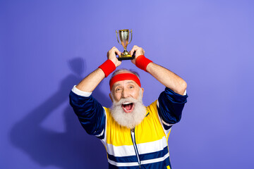 Fototapeta na wymiar Funny man celebrating victory while holding a trophy in retro sportswear against a purple background