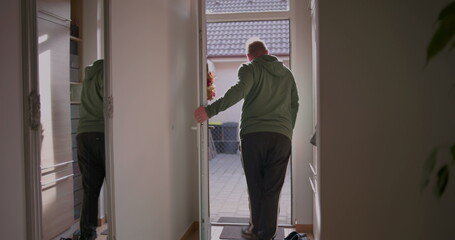 Man stepping outside through front door, leaving home for a casual outing, dressed in hoodie and sneakers, natural light illuminating entryway, modern suburban house exterior