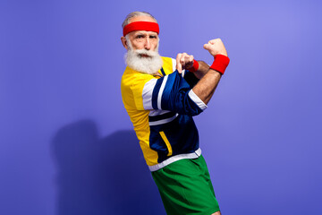 Confident senior man in retro inspired activewear flexing with enthusiasm against a vibrant purple...
