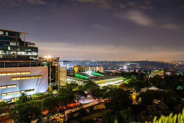 A vibrant cityscape unfolds beyond rows of apartment buildings at sunset, bathed in warm golden light; dramatic shadows and glowing skies create a cinematic urban landscape with soft bokeh detail.
