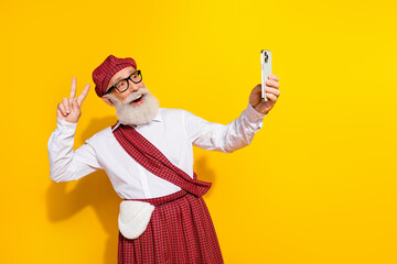 Mature man in traditional plaid attire taking a cheerful selfie against a vibrant yellow background...