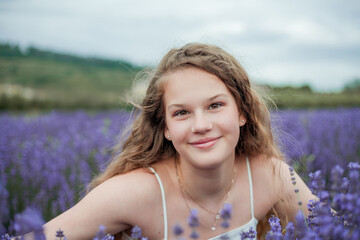 Portrait of happy girl near lavender. Curly model 13 years old with long hair in field of purple flowers. Summer.