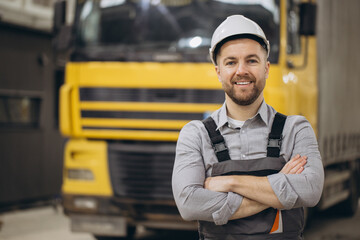 Smiling engineer wearing hardhat and overalls posing with crossed arms in front of truck