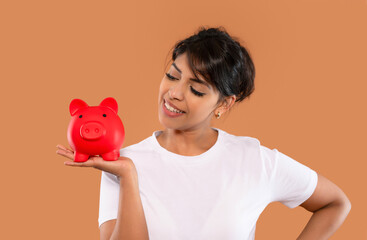 Woman smiling and holding a red piggy bank while promoting financial savings and smart money management in a cheerful indoor setting