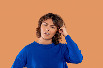 Woman in blue sweater expressing confusion while touching her head against a peach background...