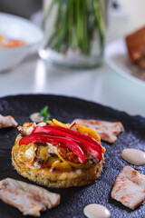 Slices of cooked turkey with potato tortilla and red bell peppers on a black plate with sauce. Beautiful presentation of dinner.