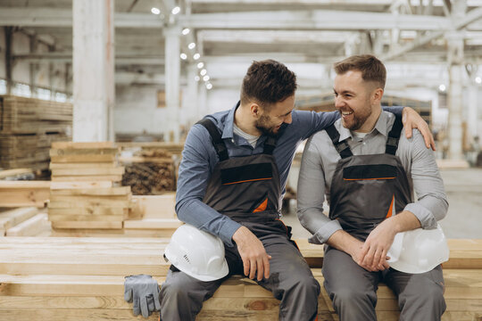 Two happy construction workers resting on wood beams in factory