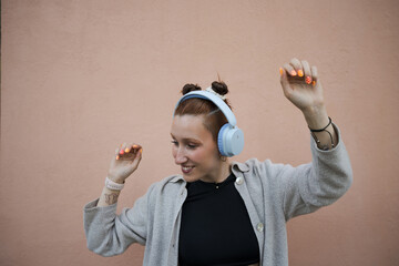 Young woman listening to music with headphones is dancing against a pink wall