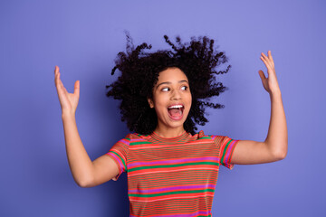 Cheerful young woman in a colorful shirt joyfully posing against a vibrant violet background with...