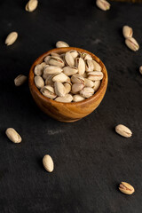 pistachio in their shells with added salt, fried unpeeled pistachio nuts in a wooden bowl with cracked shells, closeup
