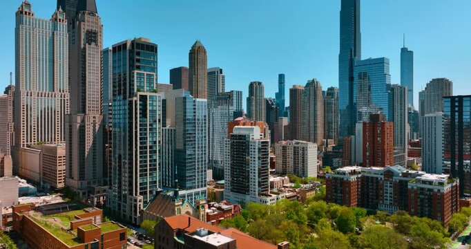 Fantastic view of diverse modern beautiful skyscrapers in the downtown of Chicago, Illinois, USA. Drone footage over the low-rise buildings among the lush greenery.
