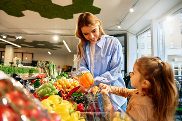 Happy mom and daughter choosing bell pepper in grocery store