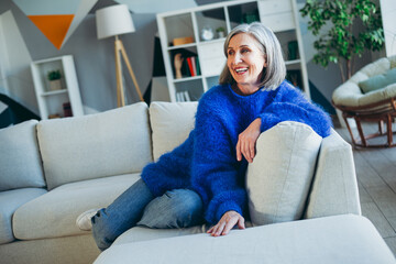 Obraz premium Smiling elder woman enjoying a relaxing moment on a cozy sofa in a brightly lit modern living room interior