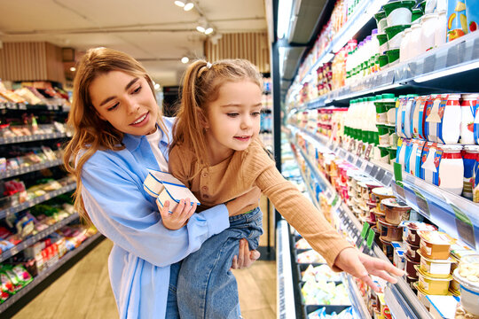 Mother and daughter choosing dairy products together in supermarket refrigerator aisle