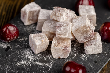Turkish delight with cherry on a black slate board, cubes of sweet Turkish delight with powdered sugar