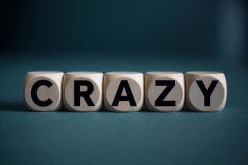 Obraz premium Wooden cubes spelling word crazy on teal background, showcasing concept of unconventionality and spontaneity