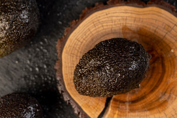 wet black avocado fruits of small size on a black slate, ripe avocado fruit in drops of water