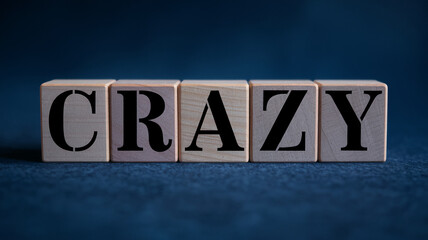 Fototapeta premium Wooden blocks spelling CRAZY on dark background, showcasing a concept of madness, excitement, or unpredictability