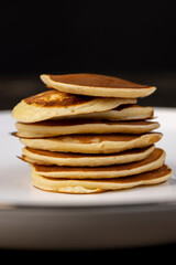 a large number of delicious pancakes stacked together on a bowl, a tower of small milk pancakes on a ceramic bowl, closeup