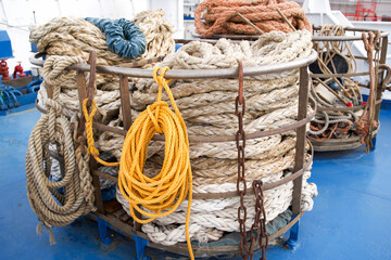 Coiled ropes of various textures and colors are neatly arranged in a circular storage container on a boat deck, showcasing maritime equipment and the essence of nautical craftsmanship